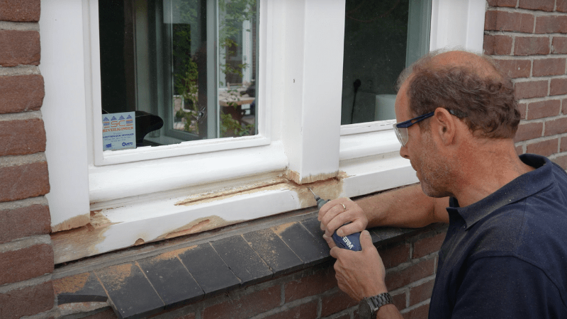 Man verwijdert houtrot in kozijn