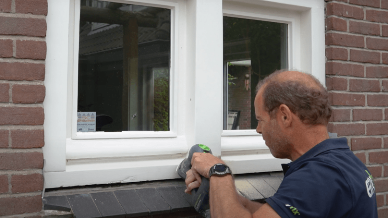 Man verwijdert verf tijdens houtreparatie in kozijn